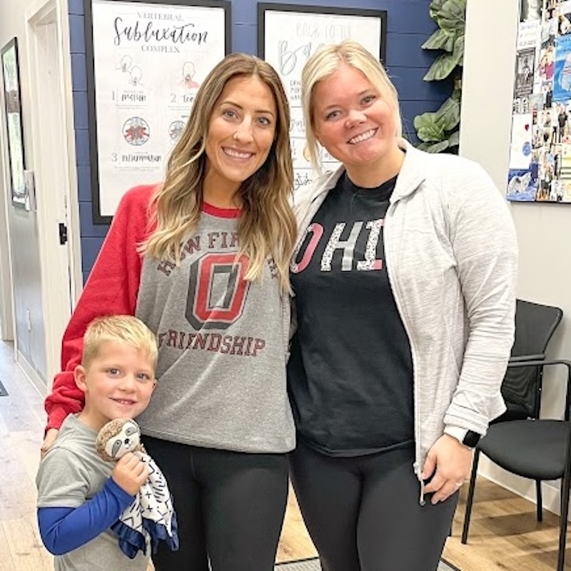 Chiropractor posing with patients and a child in a clinic, showing family-centered chiropractic care.
