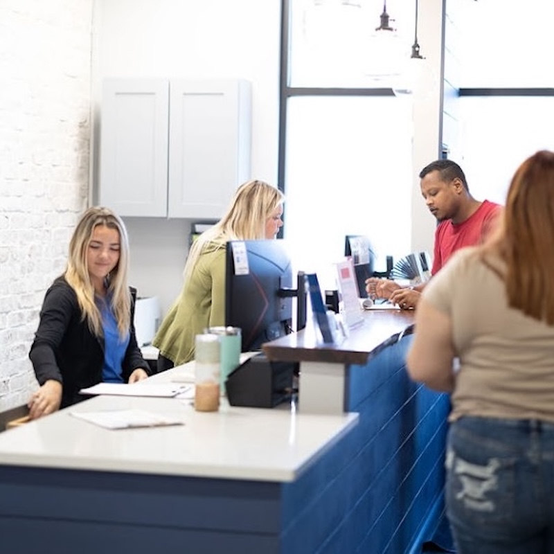 Patient at the front desk of a chiropractic clinic being assisted during check-in or scheduling.