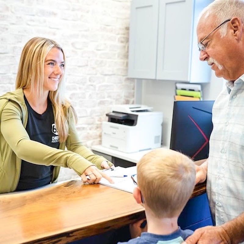 Patient and chiropractor interacting at the front desk of a chiropractic clinic during check-in or consultation.